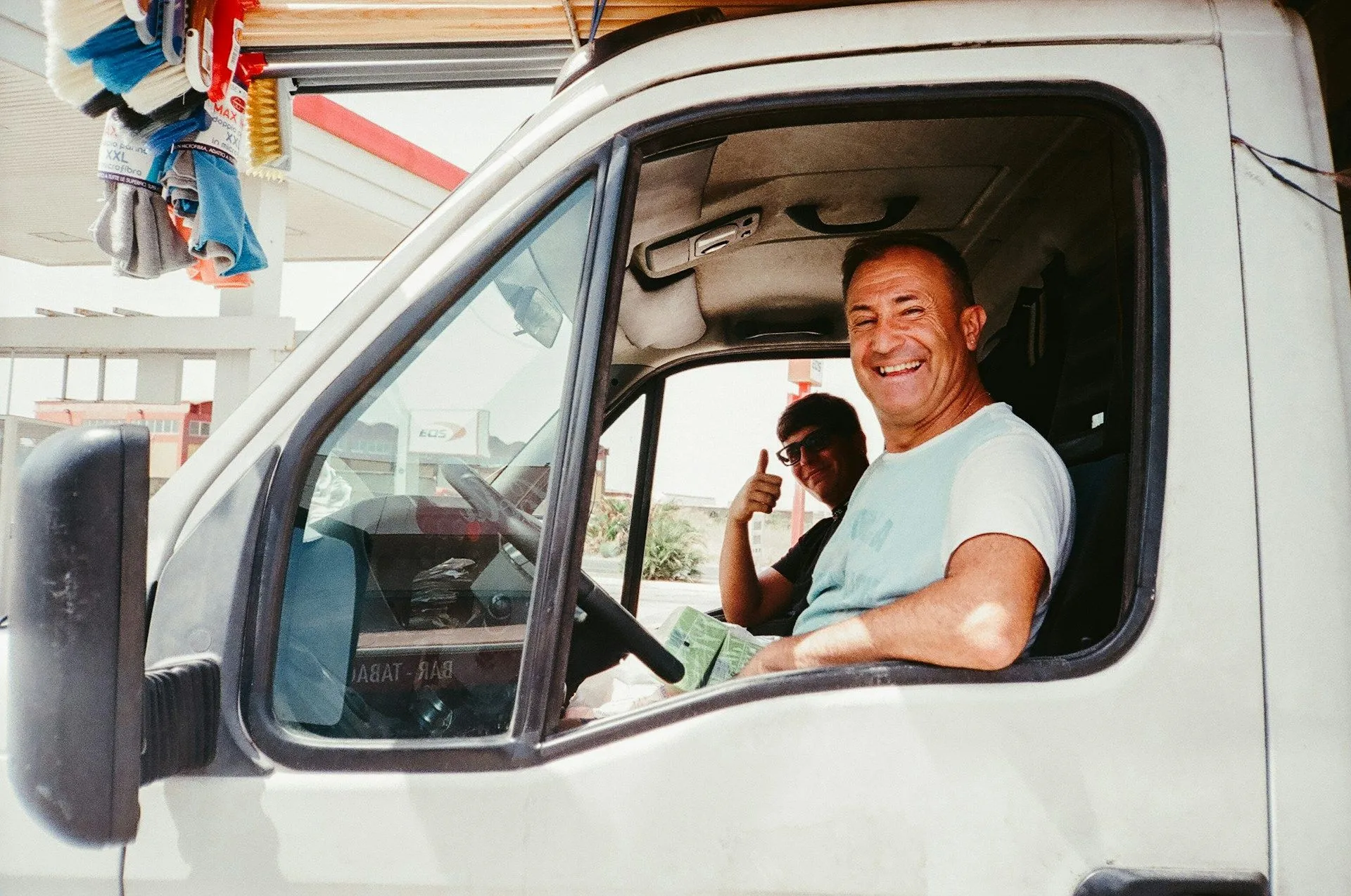Lachende chauffeur kijkt uit het zijraam van een bestelwagen, een collega steekt een duim op